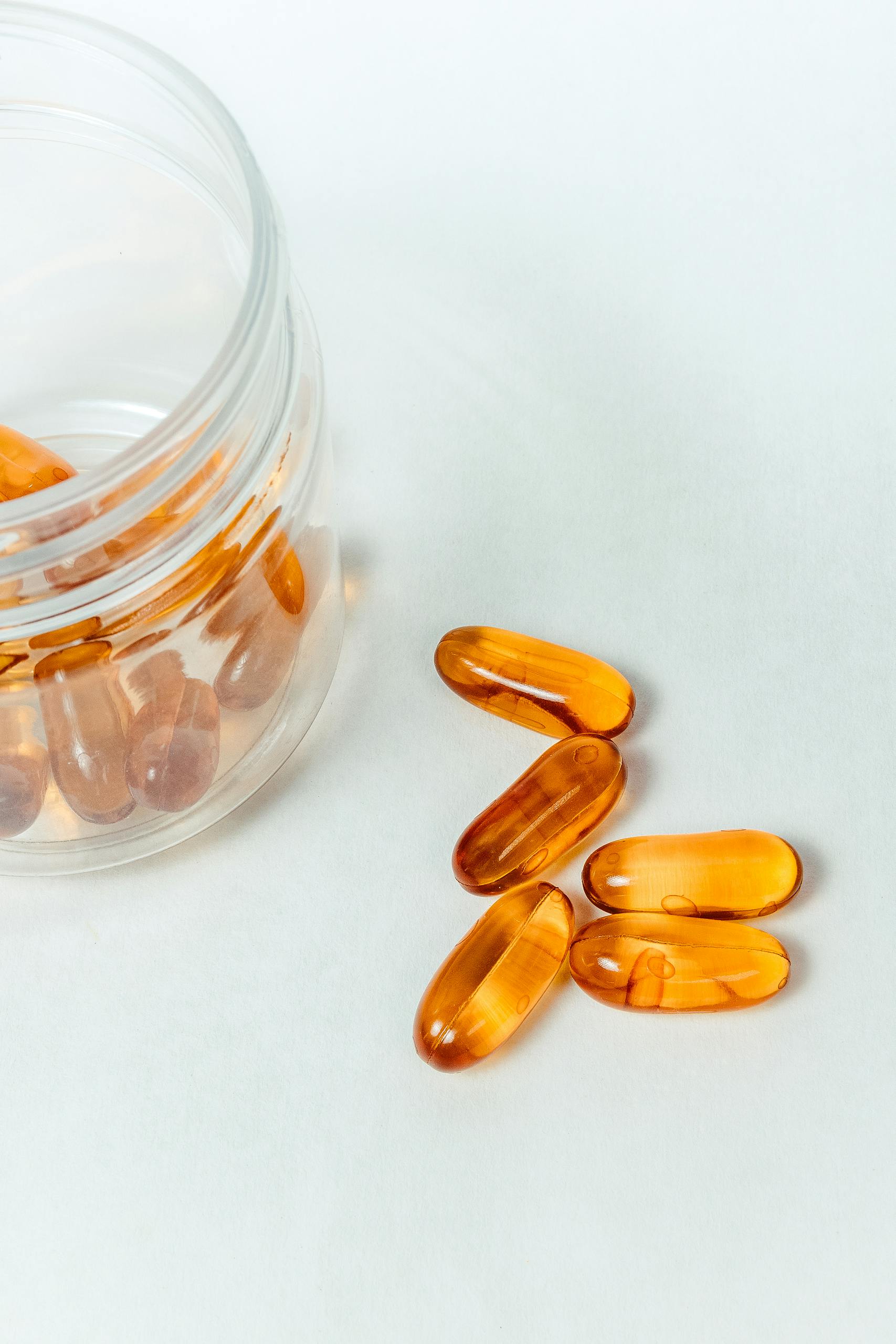 Image of transparent capsules beside an open bottle on a white background, perfect for health themes.