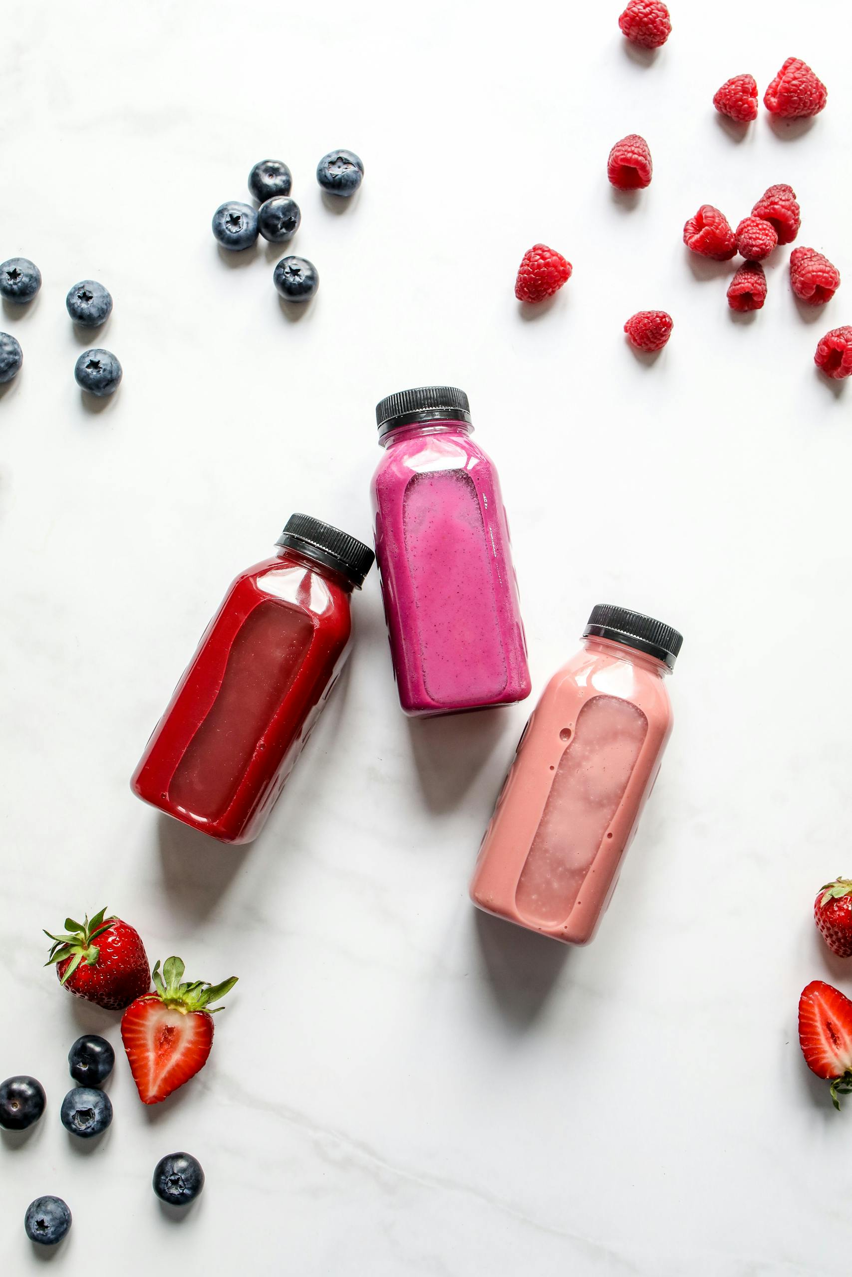How to Lose Weight Without Feeling Hungry: Overhead view of vibrant berry smoothies in bottles with scattered fresh fruits on marble.
