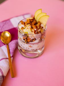 healthy eating myths: Tasty yogurt parfait with granola and apple slices on pink background.