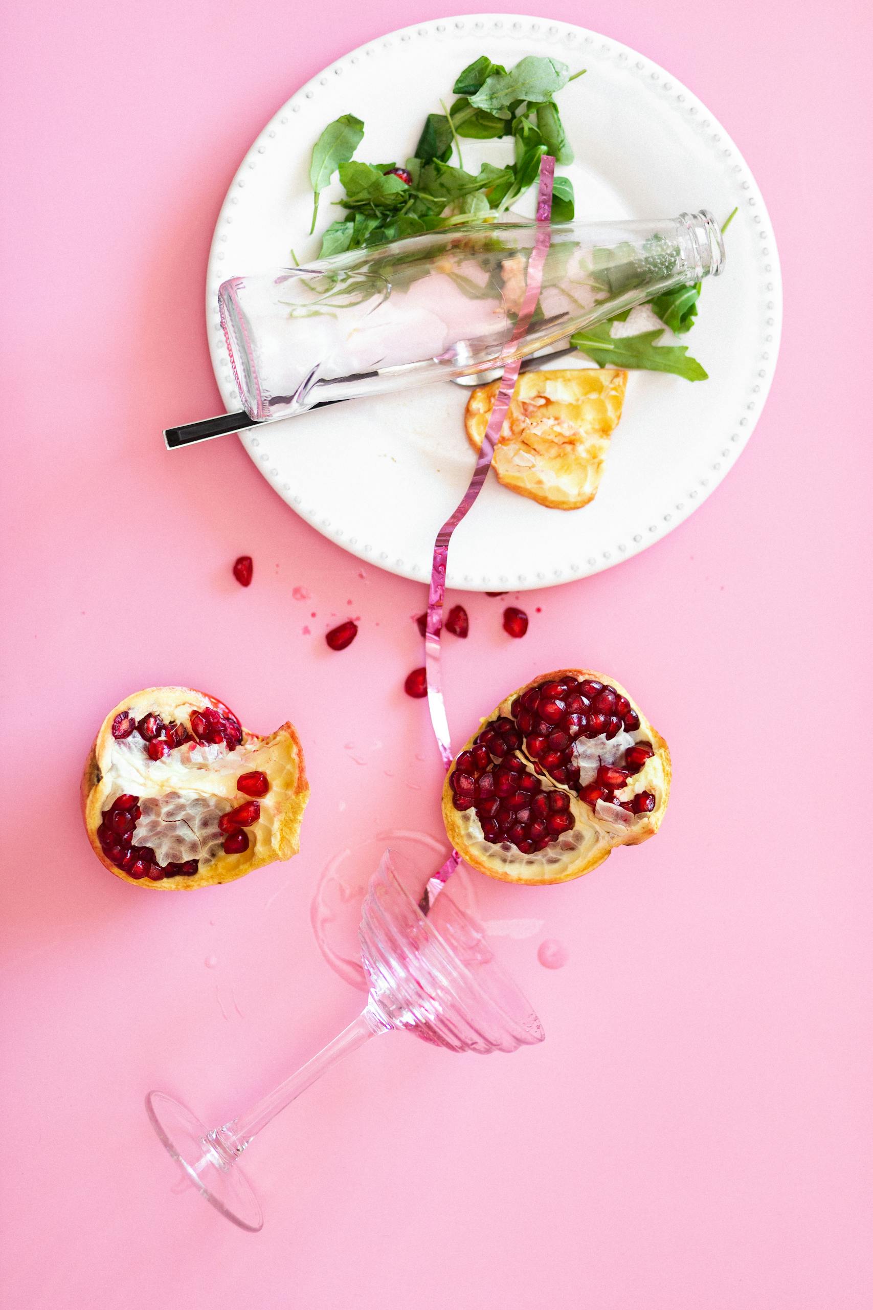 healthy eating myths: Top view of a messy party table with pomegranate and scattered food on a pink background.