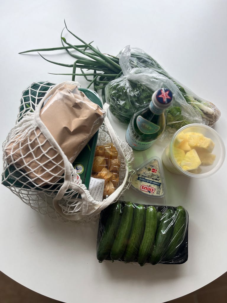 how to read nutrition labels: Top view of fresh groceries including vegetables and cheese in a mesh bag on a white table.