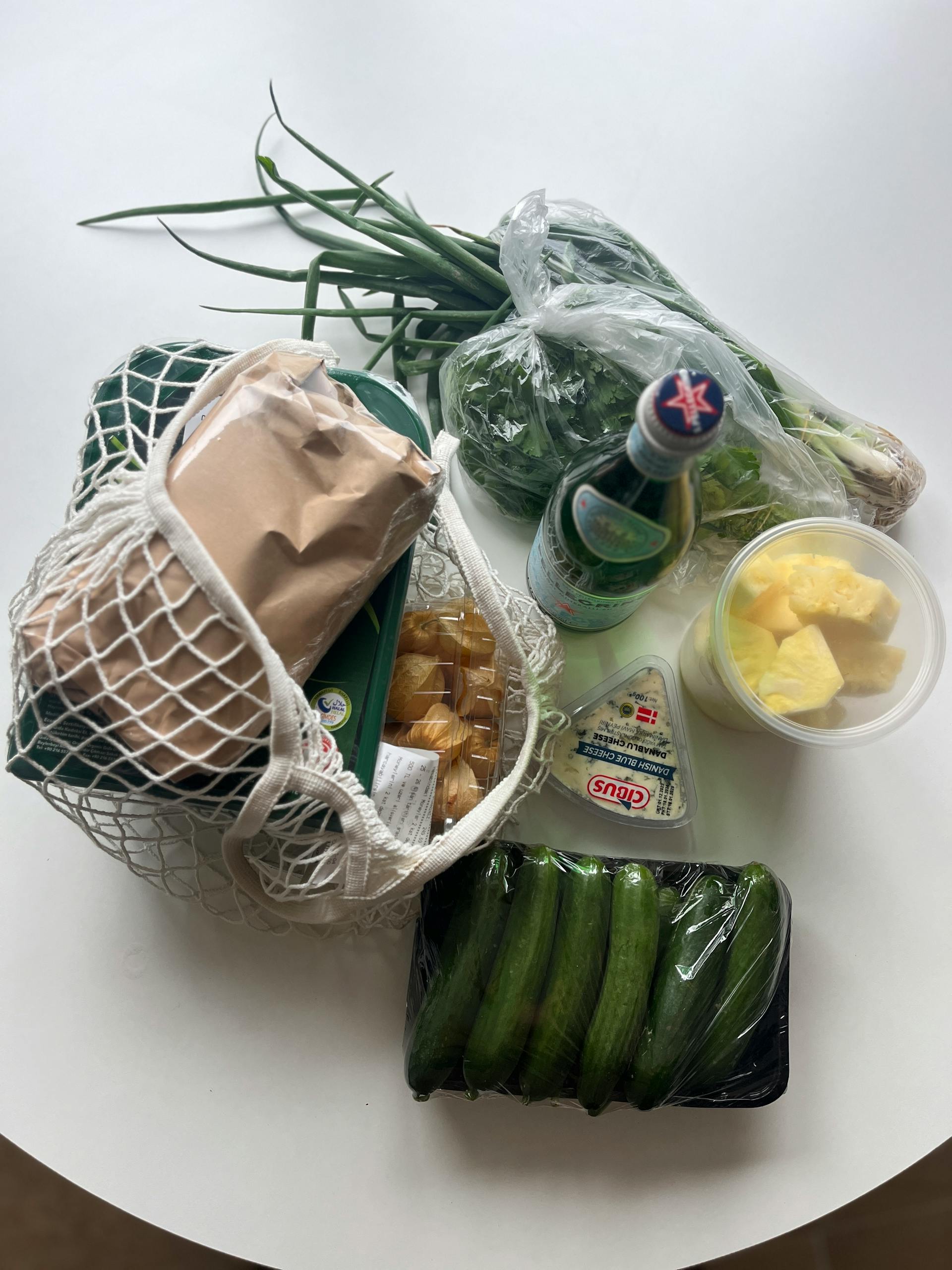 how to read nutrition labels: Top view of fresh groceries including vegetables and cheese in a mesh bag on a white table.