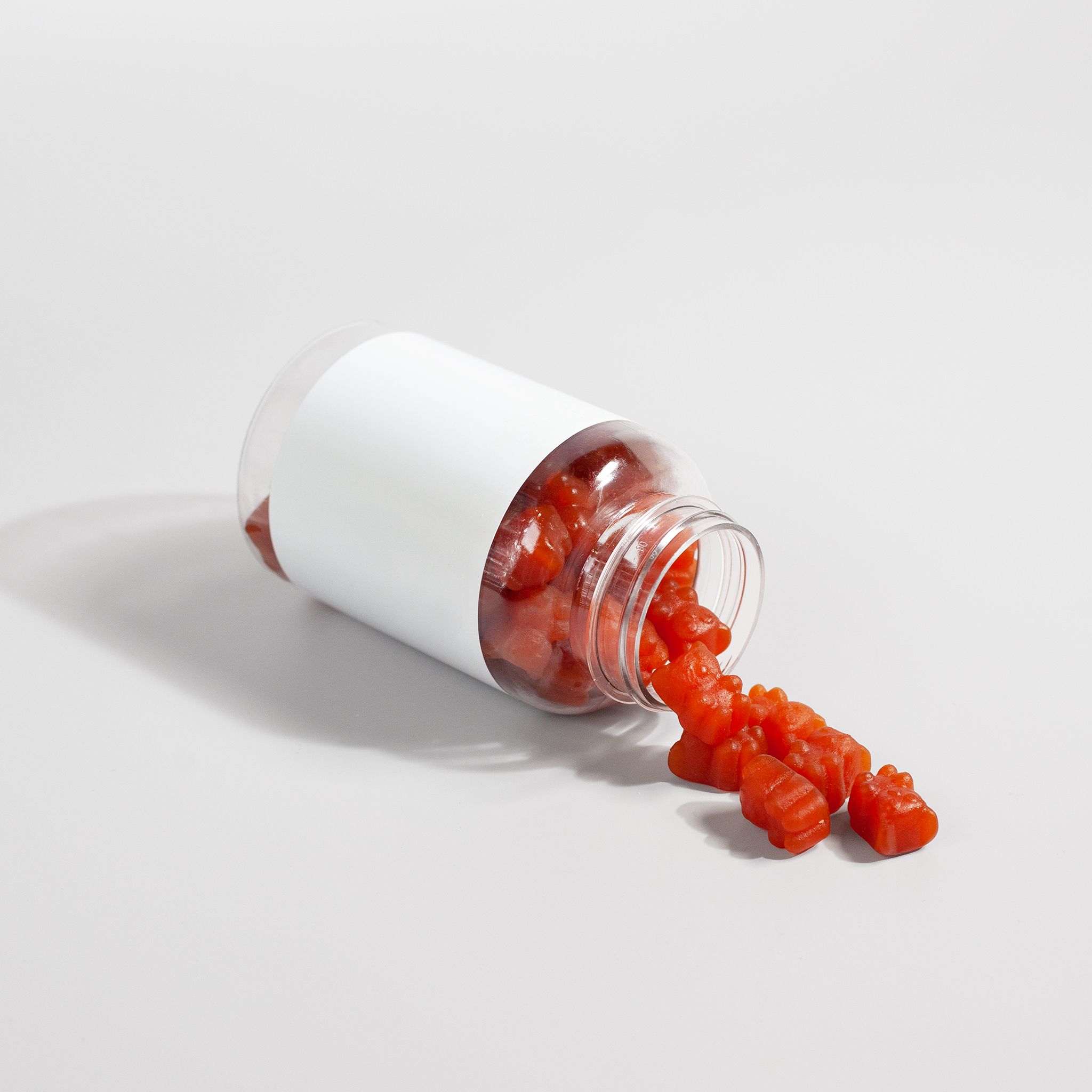 do you need a multivitamin: Close-up of gummy vitamins spilling out of a bottle on a white surface.