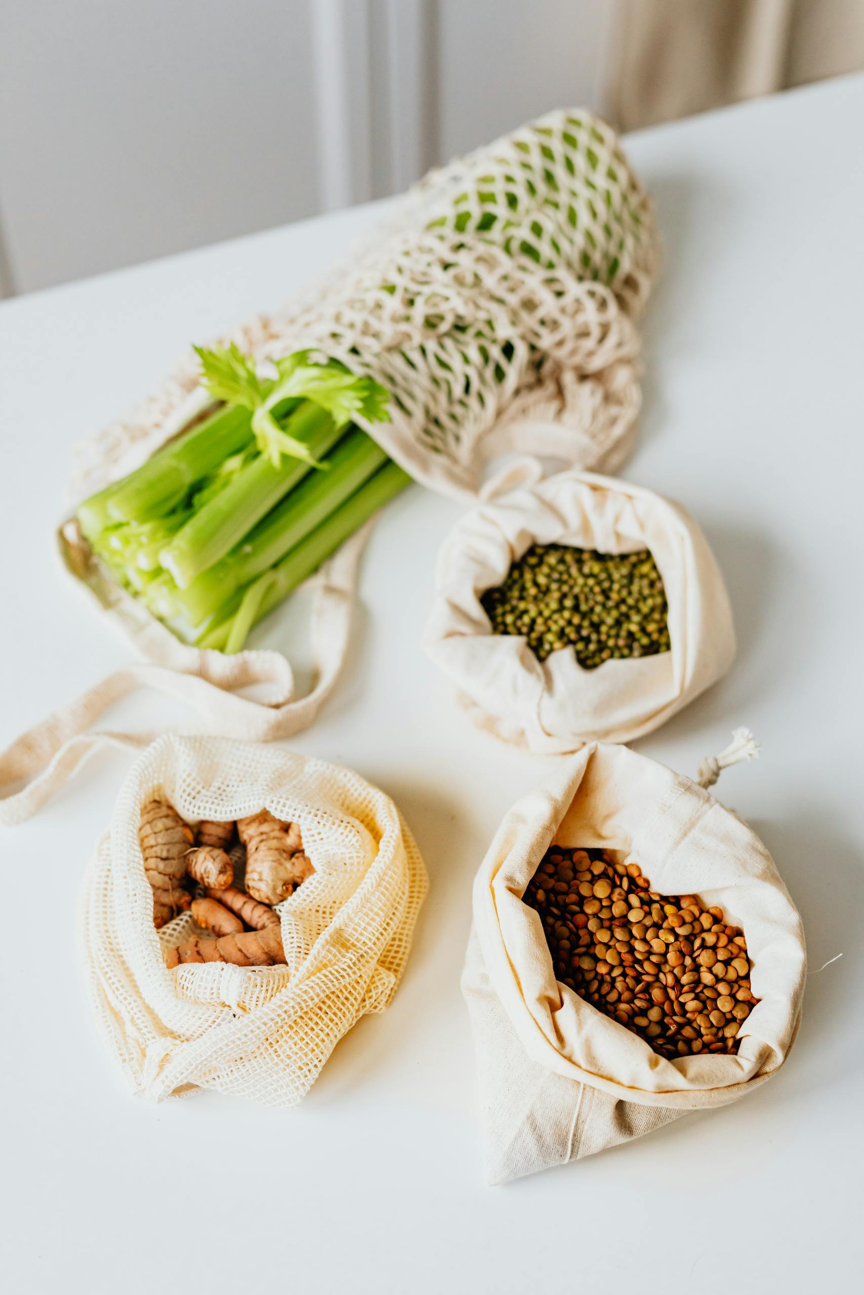 How to Reduce Food Waste at Home: Organic vegetables and grains in eco-friendly bags on a white table, promoting sustainable living.