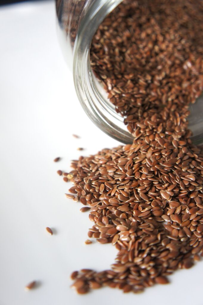 flaxseed benefits: High angle view of flaxseeds spilling from a jar onto a white surface. Perfect for health and food concepts.