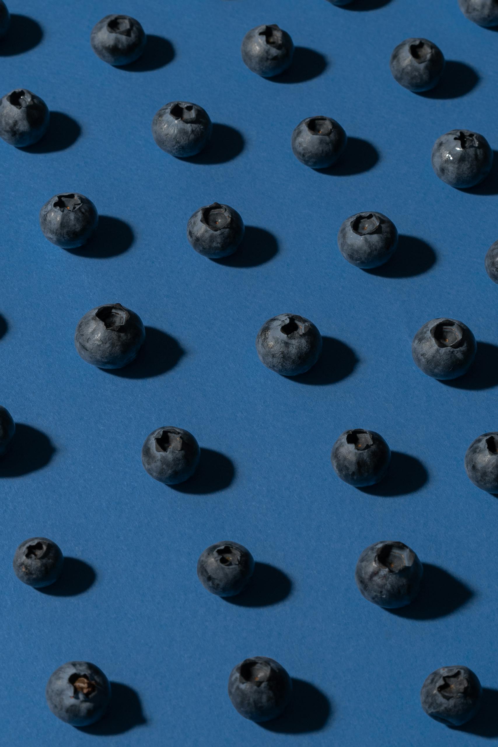 What Is the MIND Diet: Scattered fresh blueberries on a blue backdrop, offering a minimalist food composition.