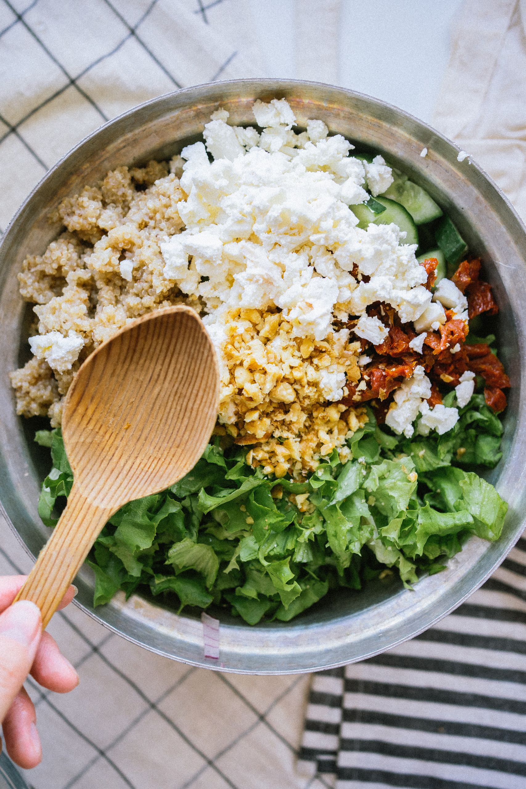 plant-based protein: Top view of a fresh quinoa salad with greens, feta, and tomatoes being mixed.