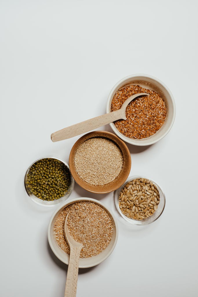 plant-based protein: Top view of assorted grains in bowls with wooden spoons on a minimalist background.