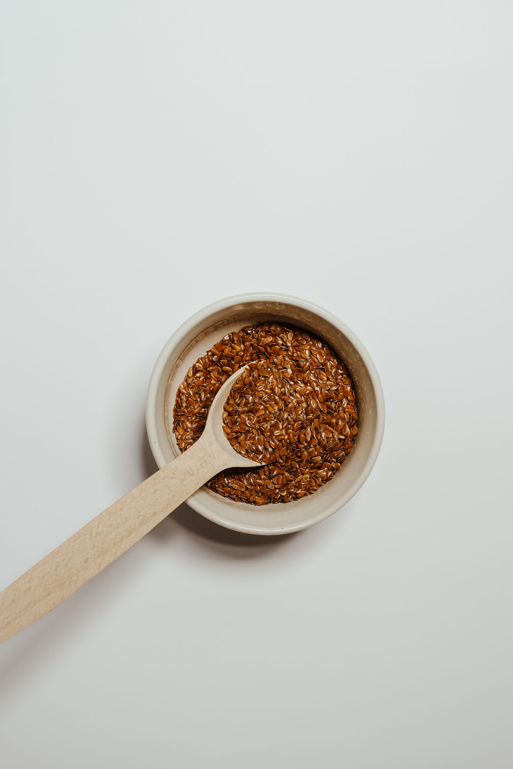flaxseed benefits: Top view of flaxseeds in a bowl with a wooden spoon against a white background.