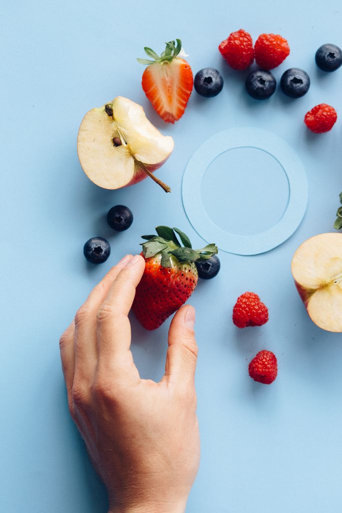 What to Eat During Menopause: Top view of fresh berries and apple slices arranged creatively with a hand reaching for fruit.