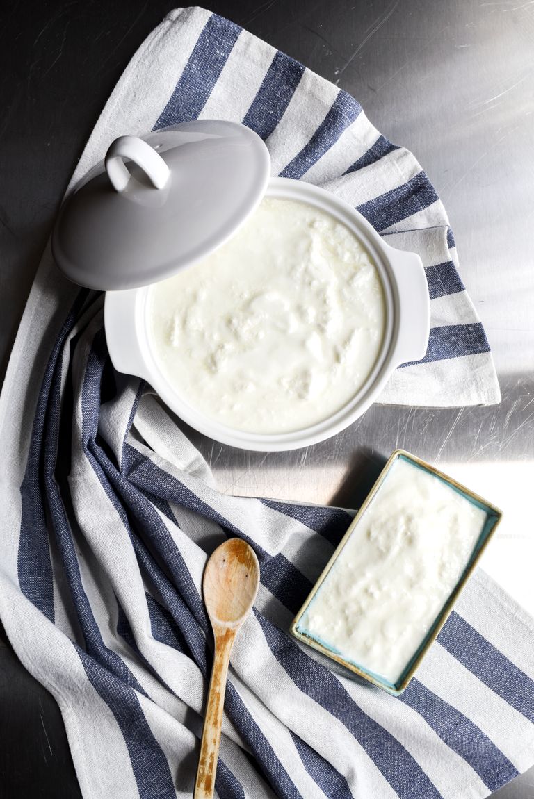 How to Introduce Allergens to Baby: Top view of homemade yogurt in a ceramic pot, styled with a wooden spoon and striped cloth.
