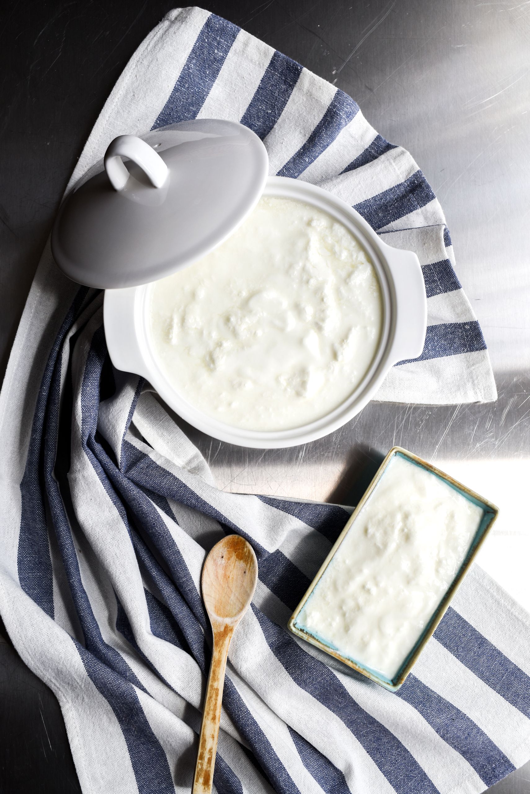 How to Introduce Allergens to Baby: Top view of homemade yogurt in a ceramic pot, styled with a wooden spoon and striped cloth.