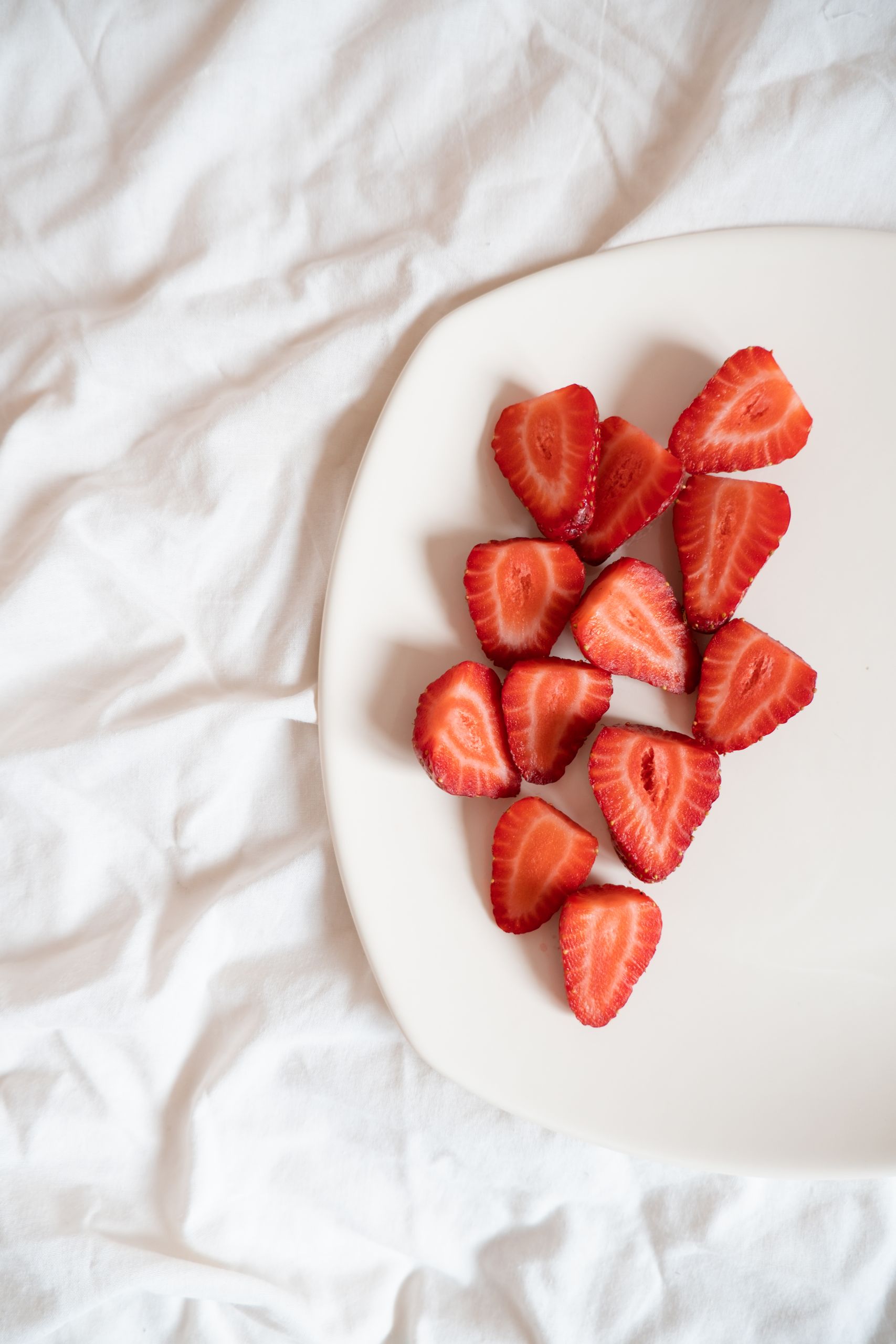Strawberry Nutrition Facts and Benefits: Top view of sliced strawberries on a plate over white bedsheet. Healthy eating concept.