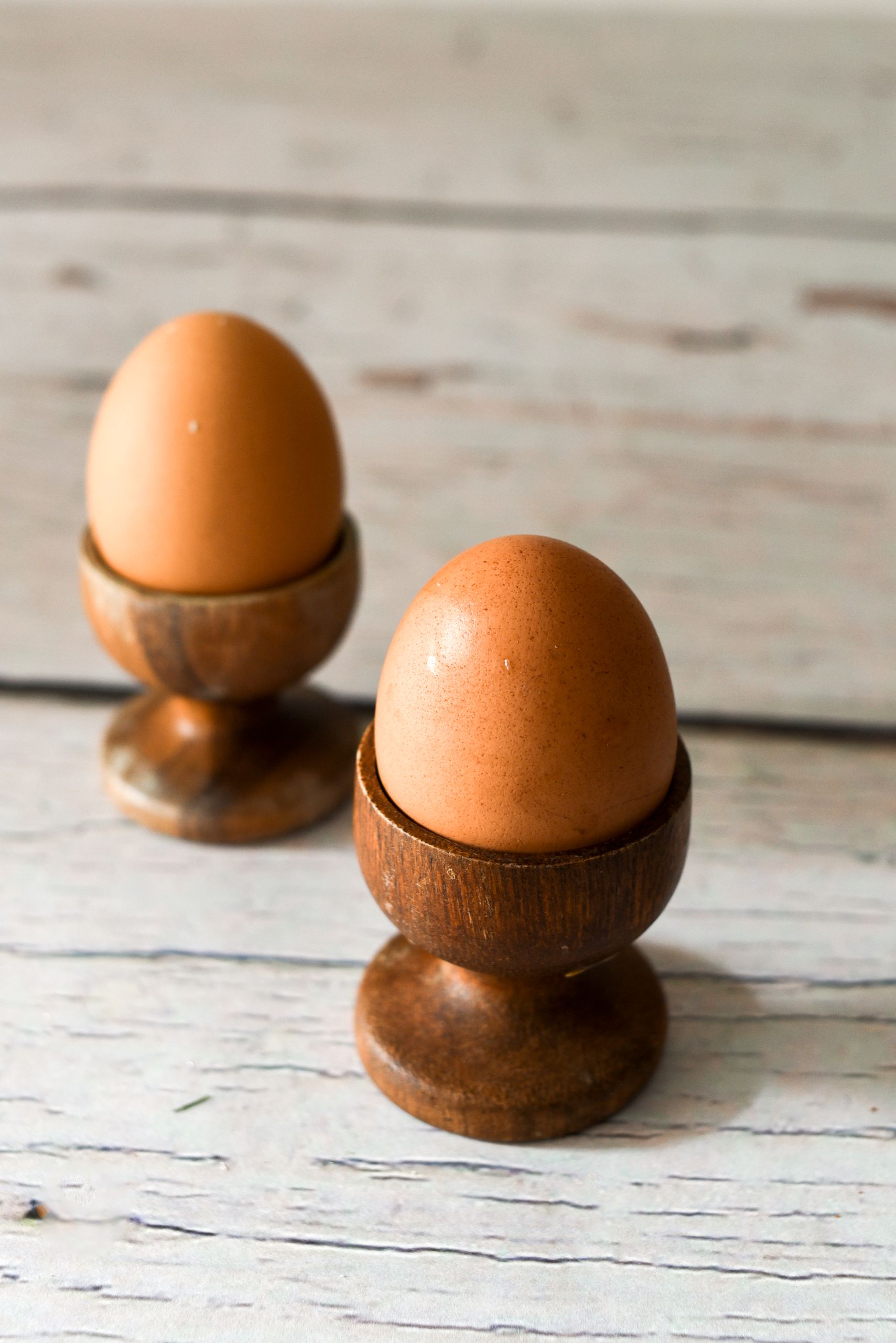 How to Introduce Allergens to Baby: Two brown eggs in wooden egg holders on a rustic wooden table surface.