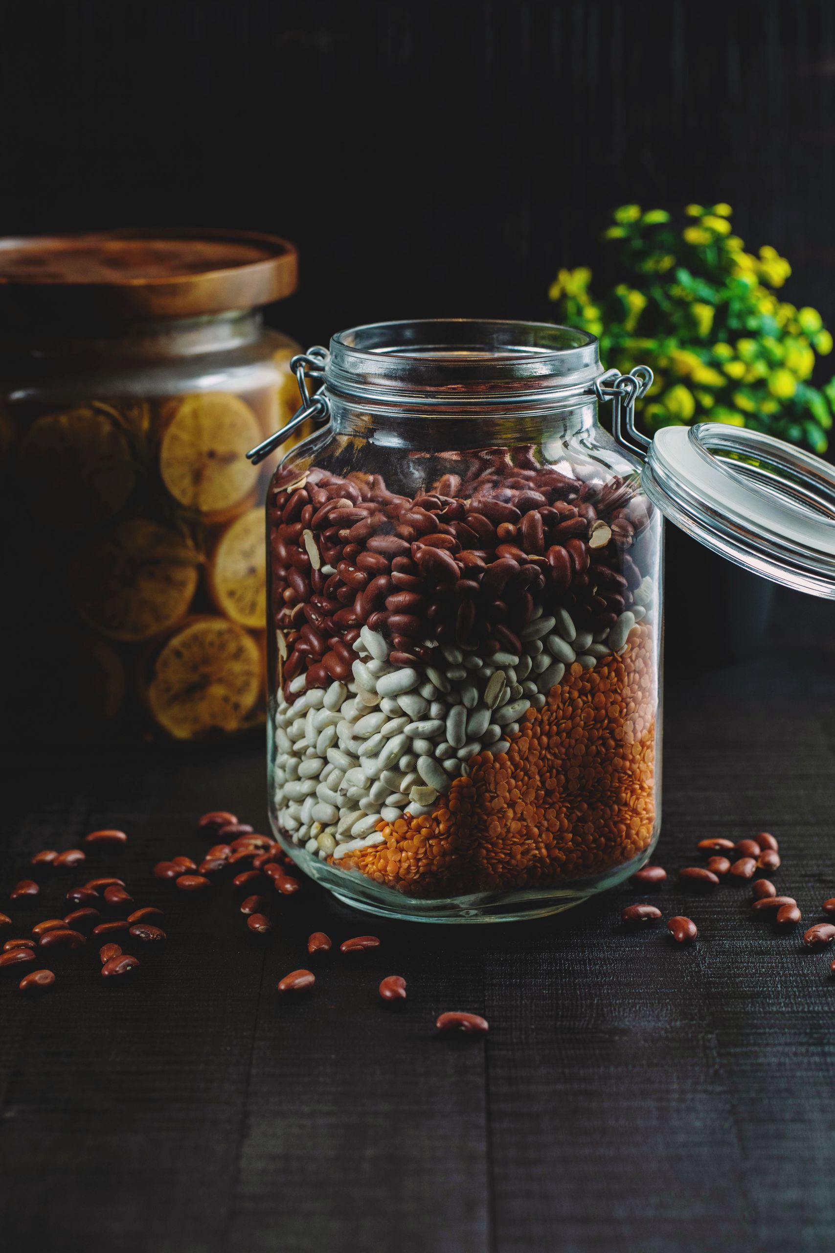 plant-based protein: Wooden table with glass jar filled with assorted white and red beans near jar with sliced oranges and plant