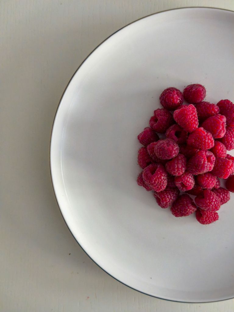 benefits of raspberries: A pile of fresh raspberries on a white plate, perfect for minimalist food photography.