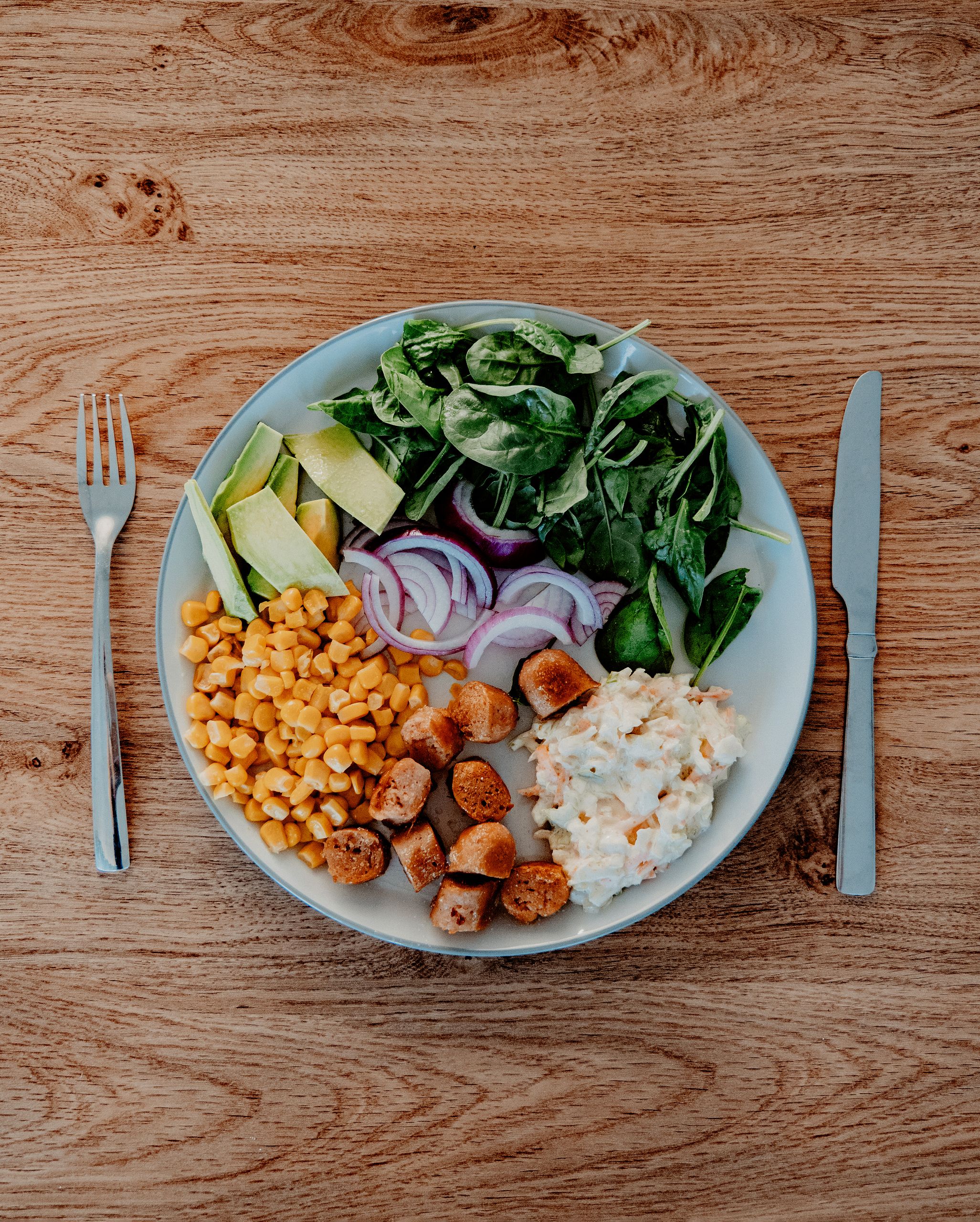 how to get enough protein on mounjaro: Delicious plate featuring avocado, corn, salad, sausages, and mashed potatoes on a wooden table.