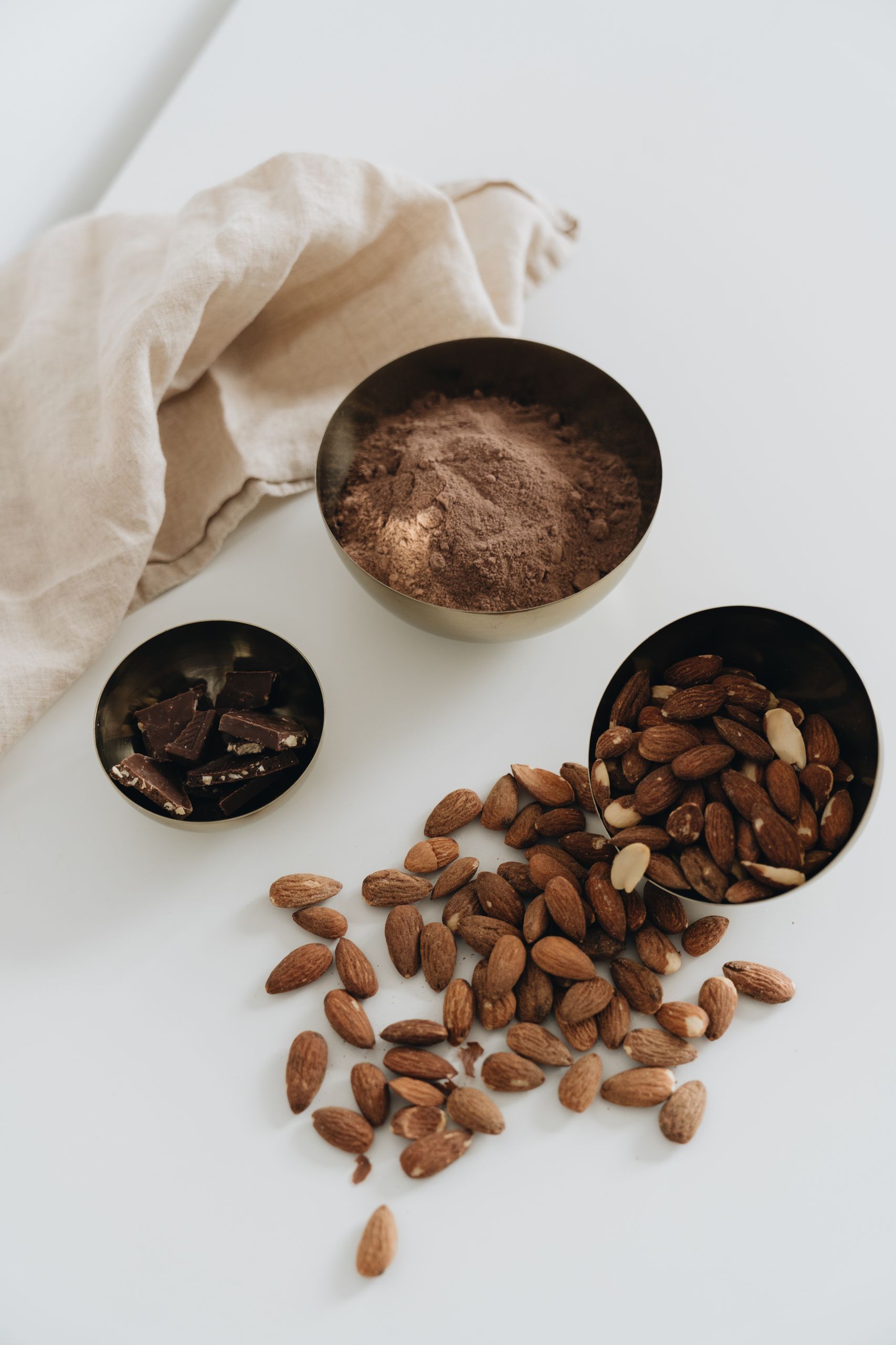 Best Foods for Muscle Gain: Flat lay of almonds, cocoa powder, and chocolate chips on white surface with cloth backdrop.