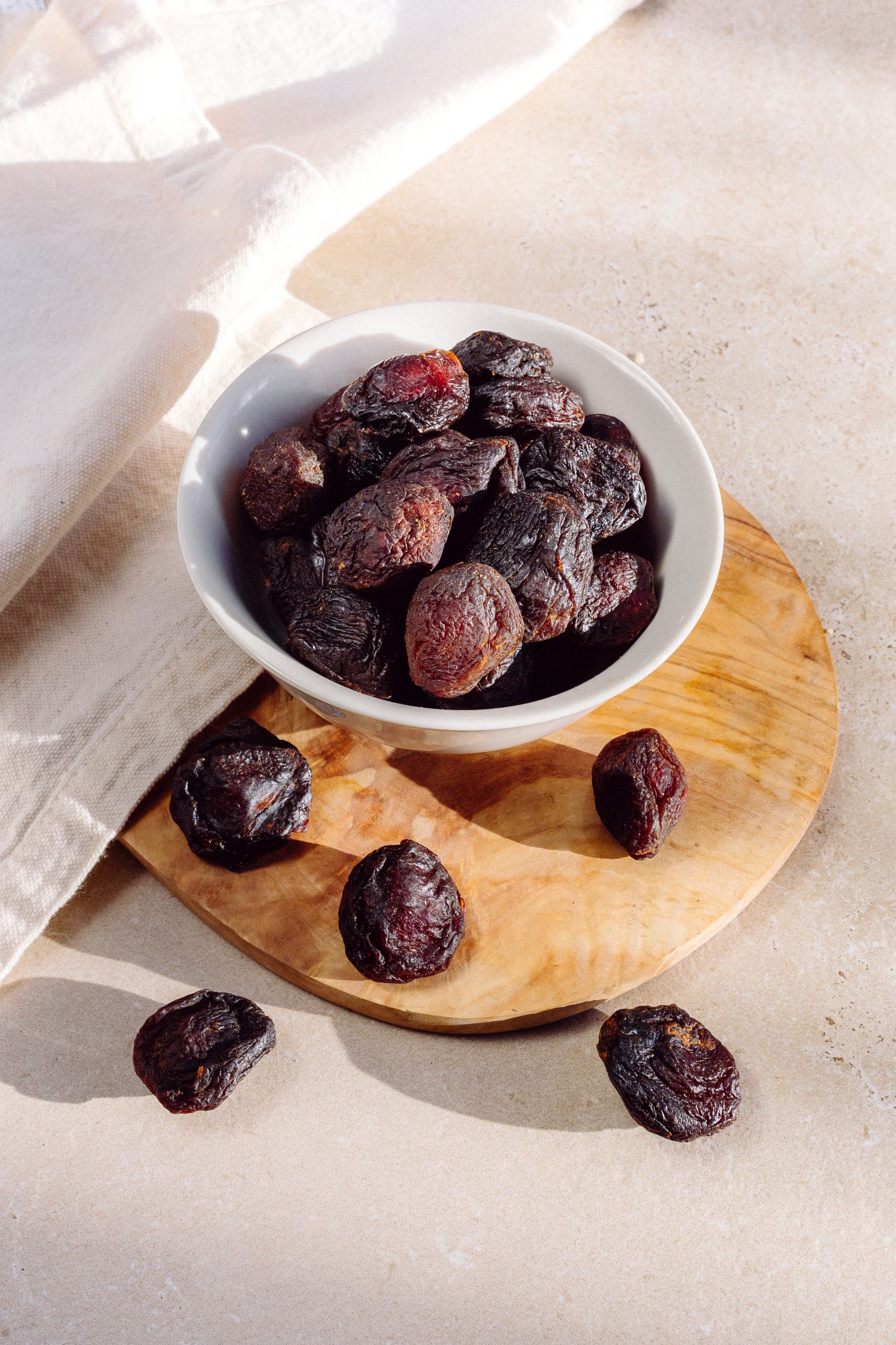 best foods for bone health: High-quality photo of dried prunes in a white bowl, set on a wooden board with natural lighting.