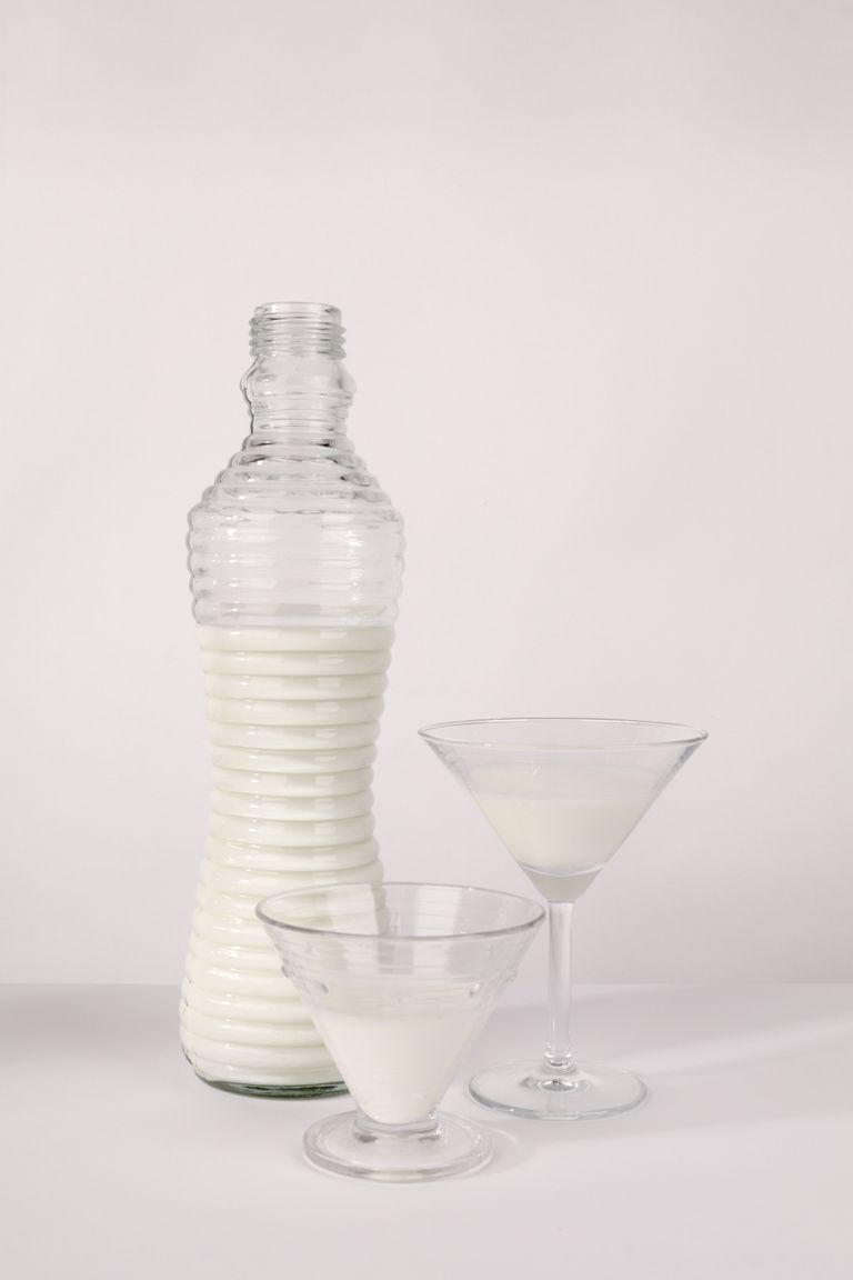 best foods for bone health: Minimalist still life of milk in a ribbed glass bottle with glasses on a white backdrop.