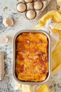 best frozen vegetarian meals: Delicious homemade lasagna in baking dish surrounded by eggs and kitchen utensils.