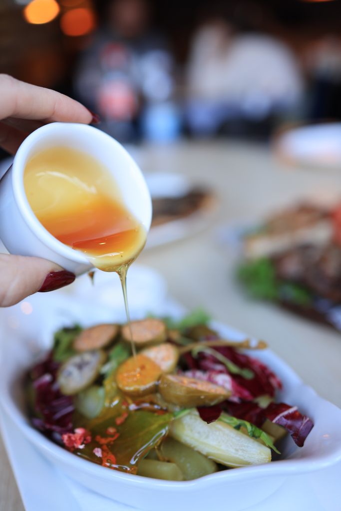 Close-up of a vibrant salad being dressed with honey mustard sauce.