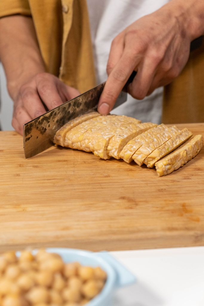 tempeh benefits: Close-up of hands slicing tempeh on a wooden board, ideal for vegan cooking themes.